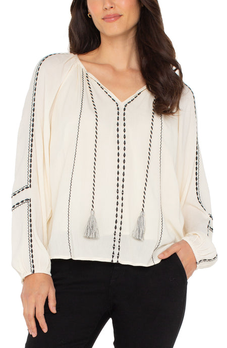 Embroidered Woven Long Raglan Slv Blouse w Tassel Tie Neck Detail